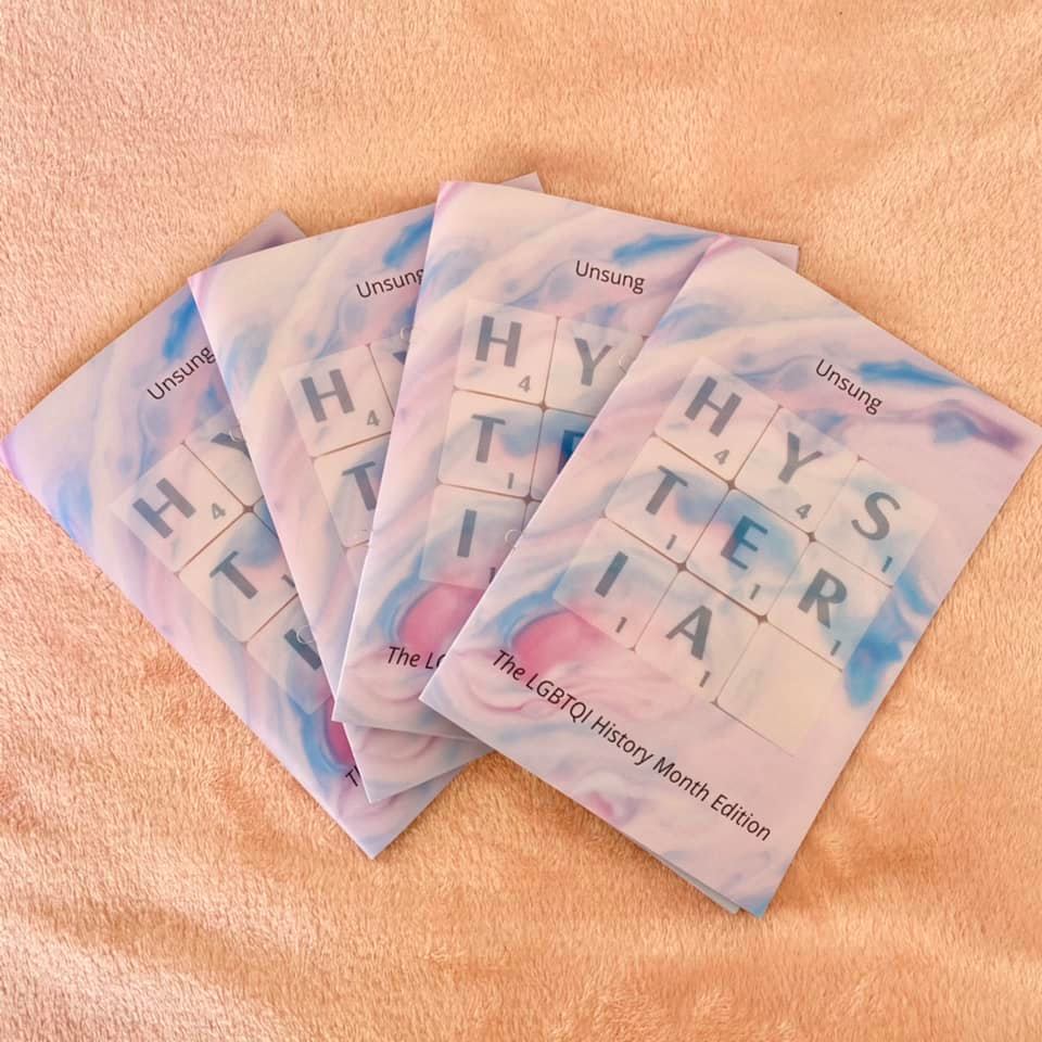 Four copies of Hysteria's LGBTQ+ History Month zine, fanned out over a textured peach background.